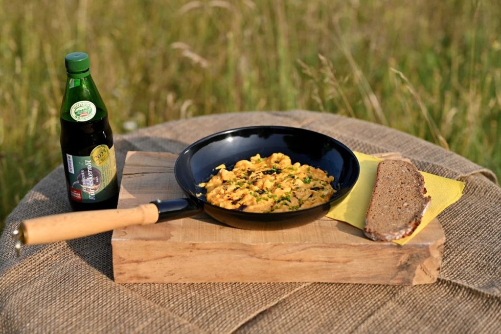 Steirische Kernöleierspeis, angerichtet in der Pfanne, mit einer Scheibe Brot als Beilage.