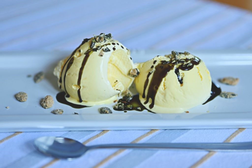 Zwei Kugeln Vanilleeis mit Kürbiskernöl auf einem Dessertteller angerichtet.